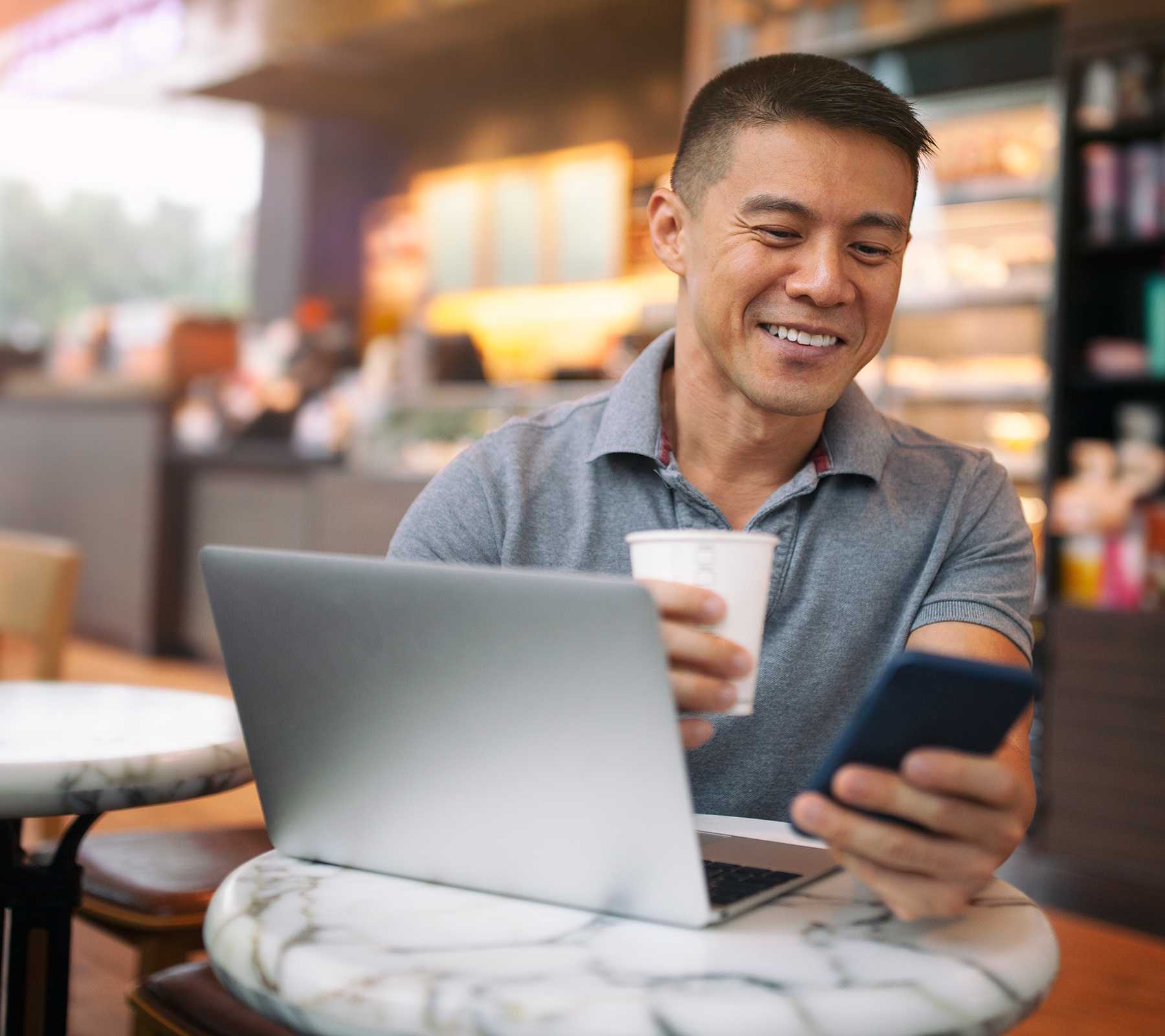 Handsome Asian man drinks a coffee whilst working in a cafe.